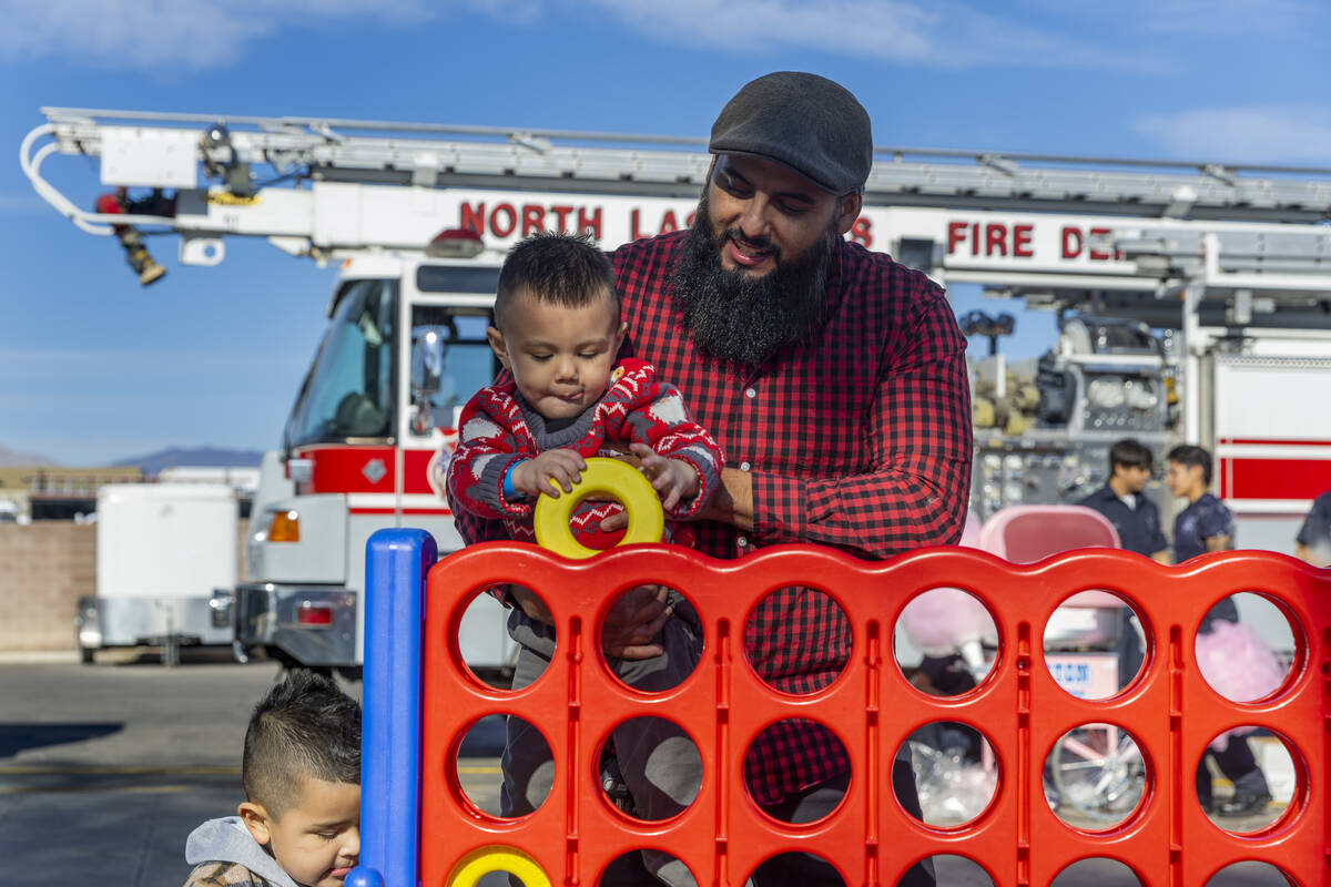 Eduardo De Los Santos helps his son Ivan, 2, to insert a ring in a large game as Gael Wence, 4, ...