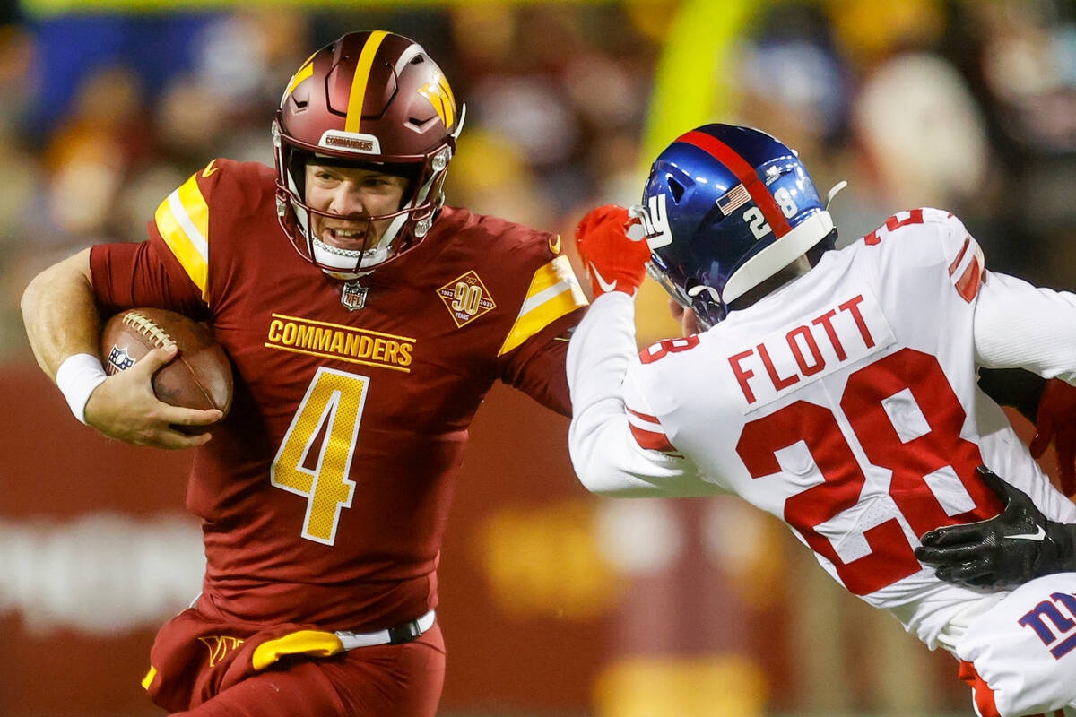 Washington Commanders quarterback Taylor Heinicke (4) stiff-arms New York Giants' Cor'Dale Flot ...