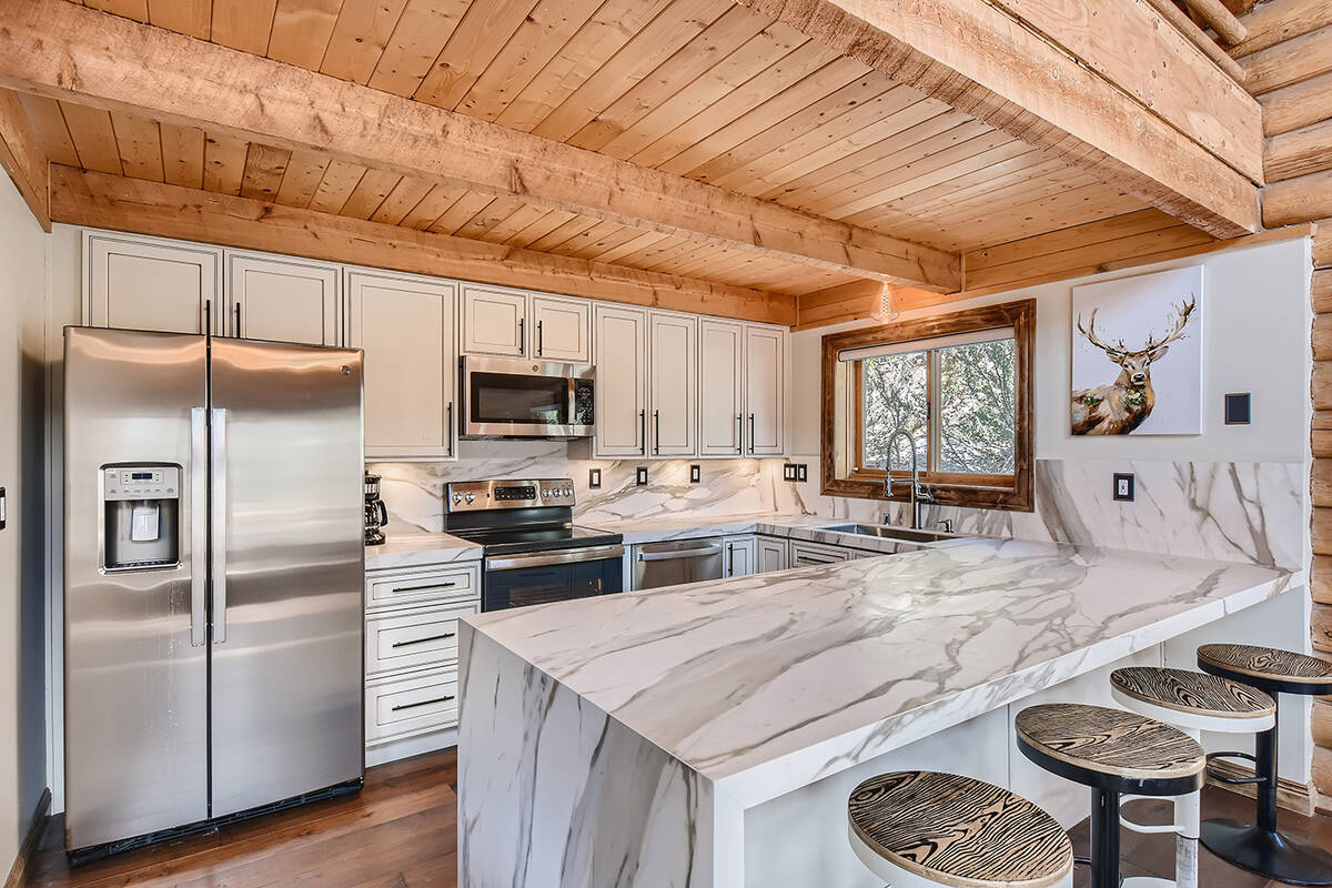 The stylish kitchen design integrates antique-white custom cabinetry complemented by rich, warm ...