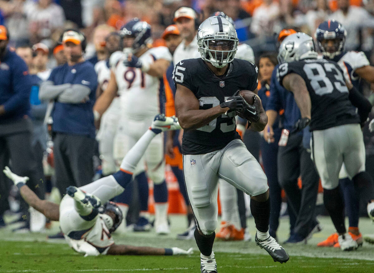 Raiders running back Zamir White (35) trips up Denver Broncos safety Kareem Jackson (22) as he ...