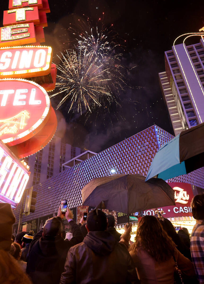 Revelers watch a fireworks and drone show above the Plaza on New Year’s Eve under a light rai ...