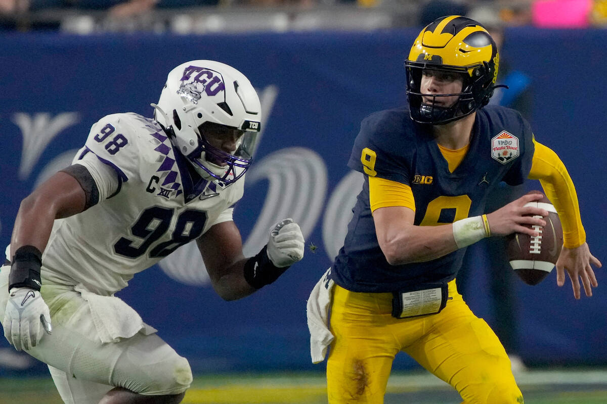 Michigan quarterback J.J. McCarthy (9) trees to elude TCU defensive lineman Dylan Horton (98) d ...