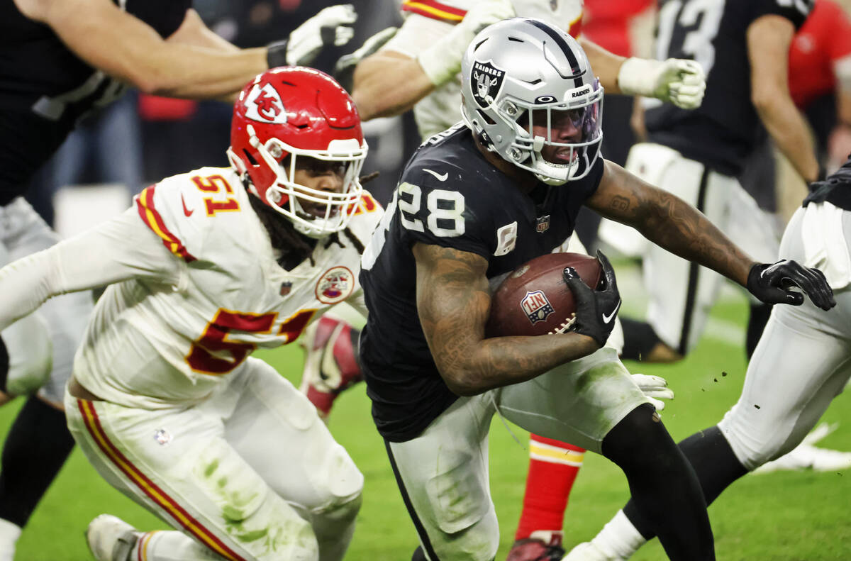 Raiders running back Josh Jacobs (28) runs the ball under pressure from Kansas City Chiefs defe ...