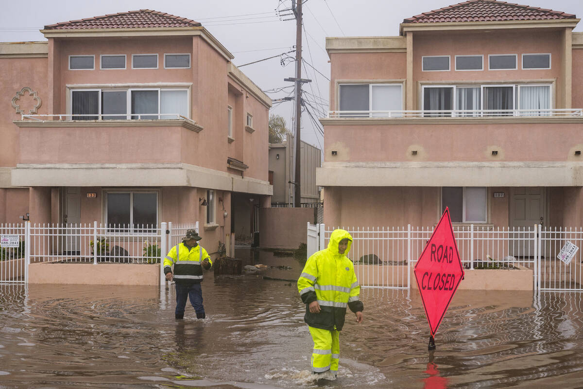 A cleaning crew walks through floodwaters in the Rio Del Mar neighborhood of Aptos, Calif., Mon ...