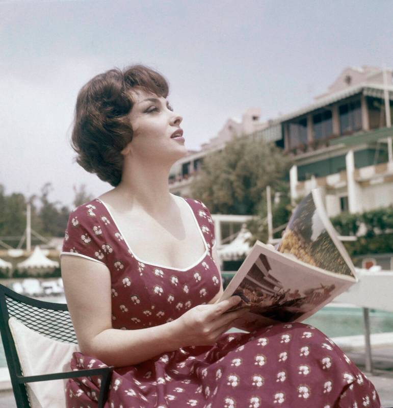 FILE - Actress Gina Lollobrigida reads a magazine as she sits by the pool during her stay at th ...