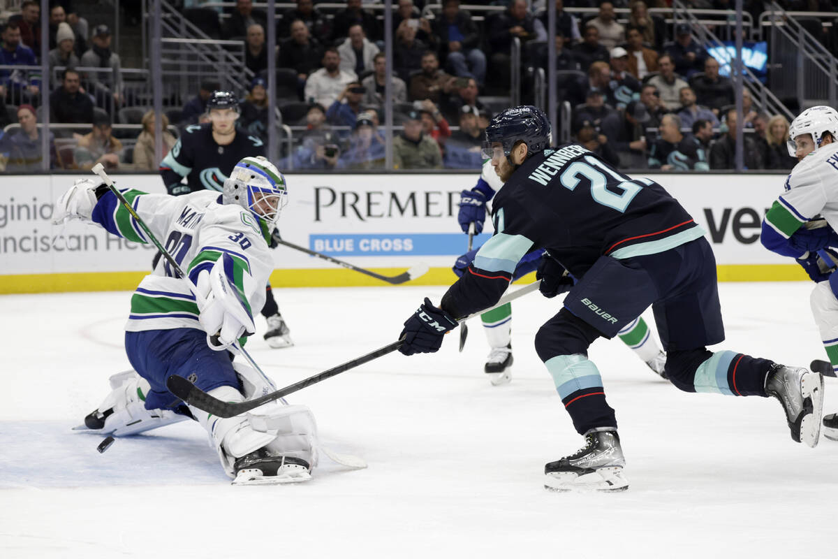 Seattle Kraken center Alex Wennberg (21) sends the puck past Vancouver Canucks goaltender Spenc ...