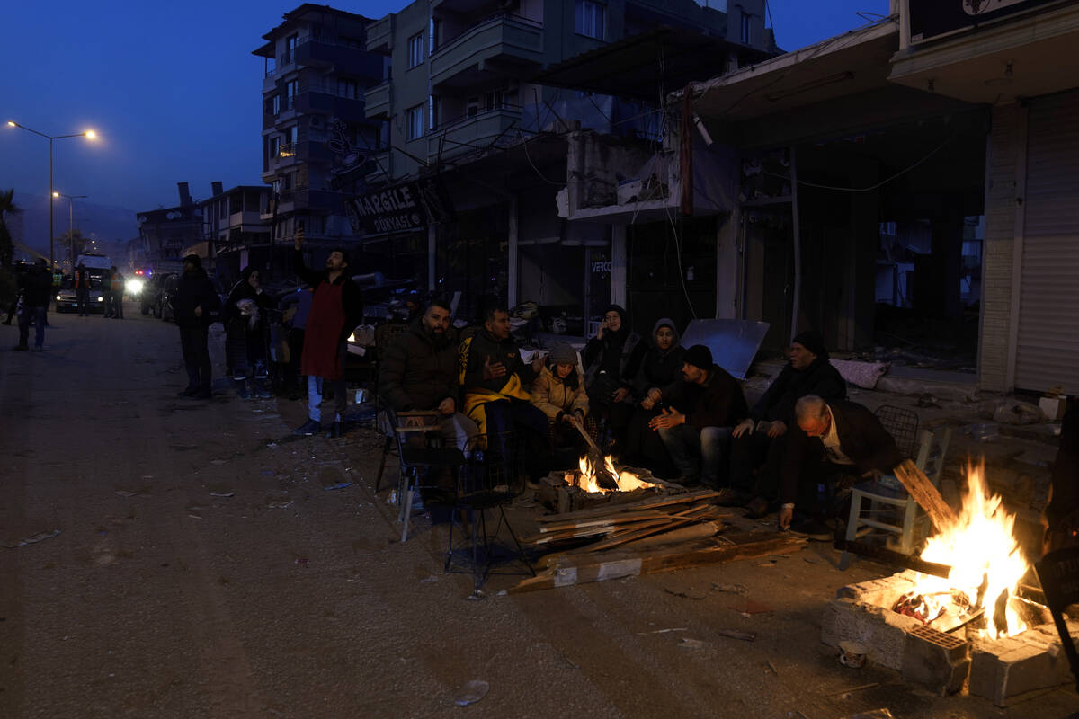 People warm up with fire next to destroyed buildings in Antakya, southern Turkey, Thursday, Feb ...