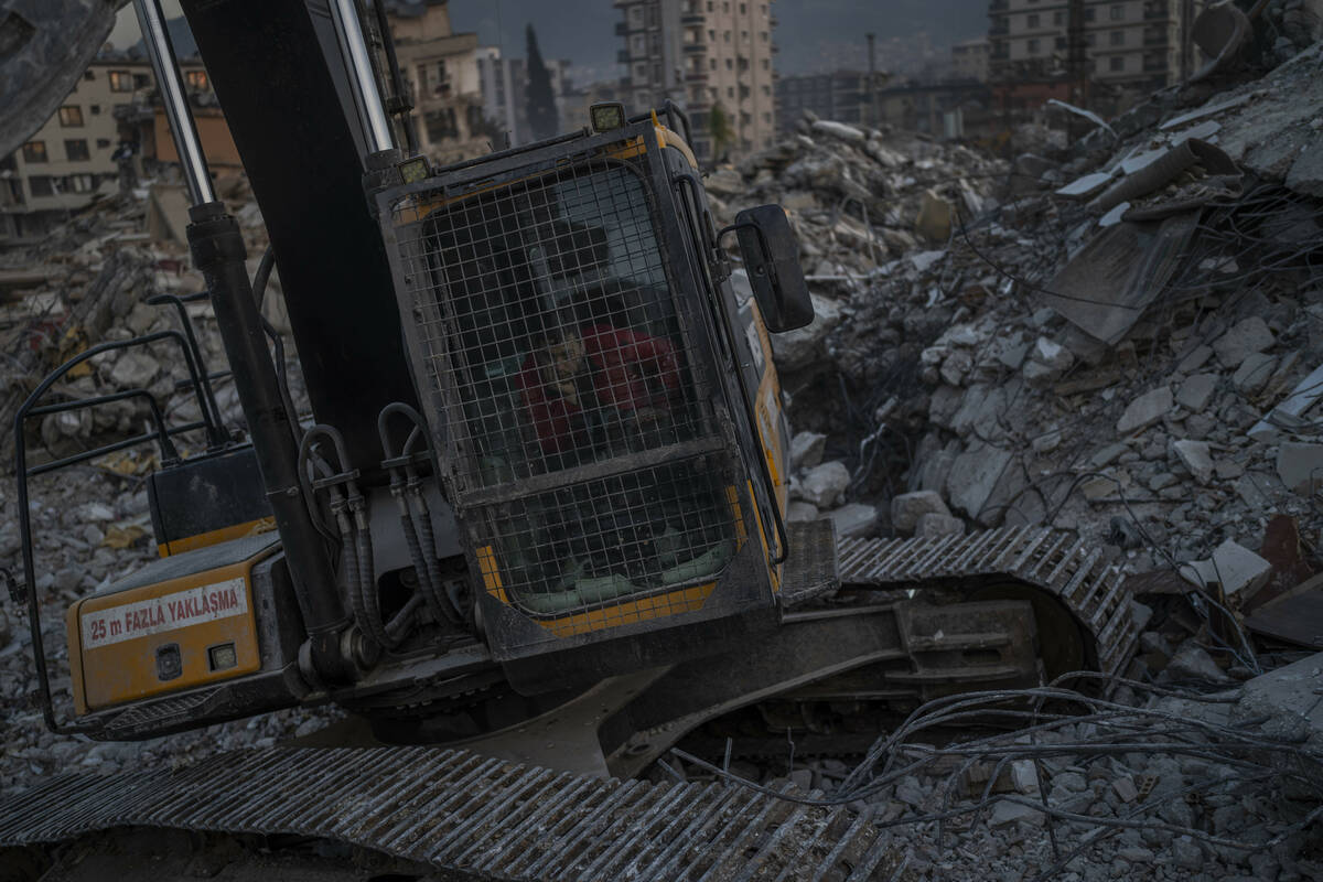 An excavator driver waits for a rescue team to recover the body of an earthquake victim from a ...