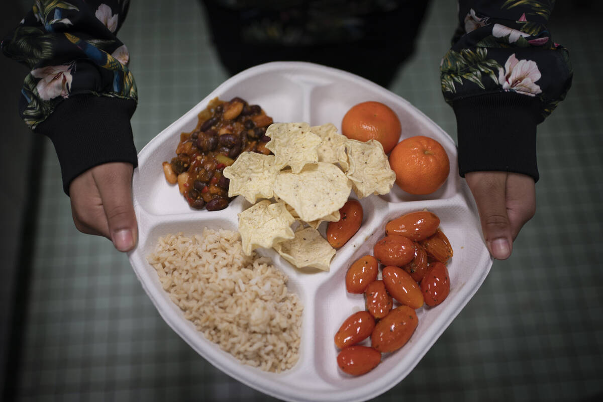 A seventh grader carries her plate which consists of three bean chili, rice, mandarins and cher ...