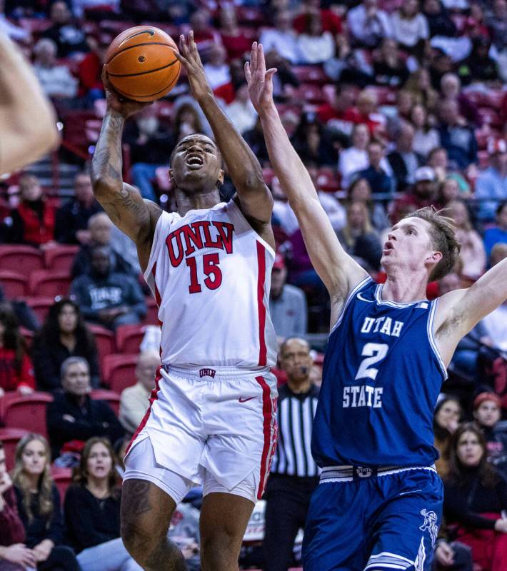 UNLV guard Luis Rodriguez (15) absorbs some contact and still shoots over Utah State guard Sean ...