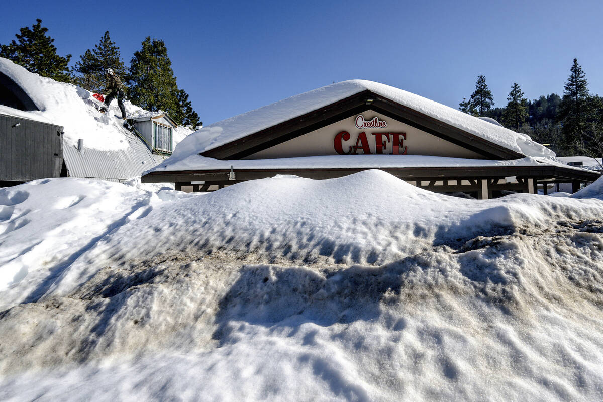 A man shovels snow off the roof of a store in Crestline, Calif., Friday, March 3, 2023, as buil ...