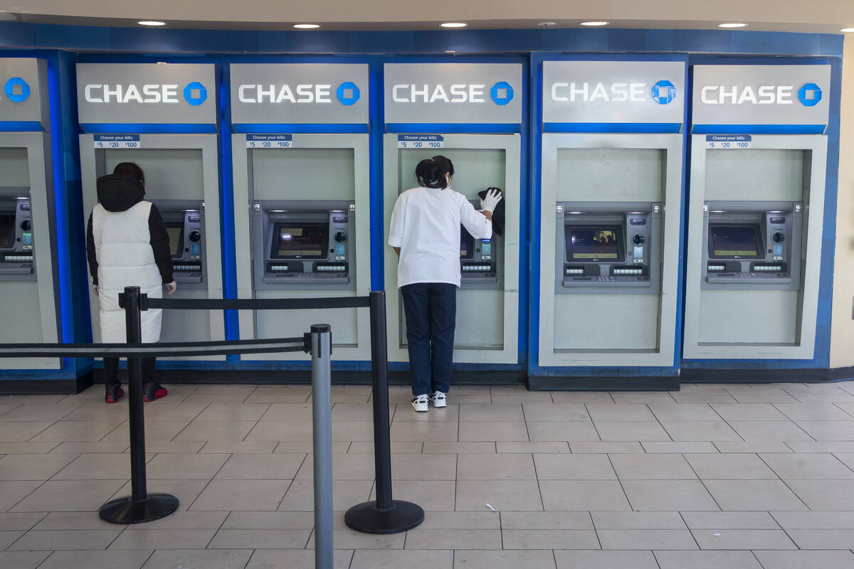 FILE - In this March 24, 2020 file photo, a Chase bank employee, right, cleans the branches ATM ...