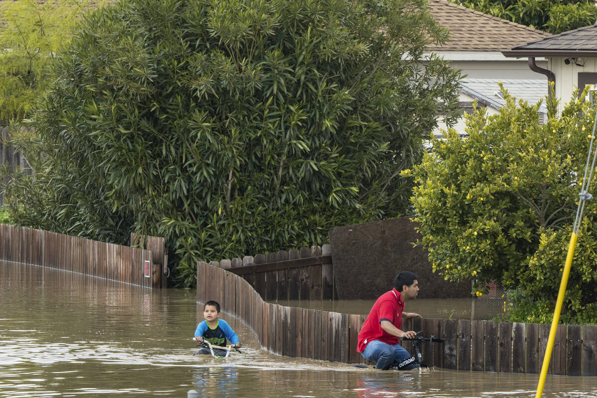 A boy and a man ride bicycles through floodwaters in Watsonville, Calif., Saturday, March 11, 2 ...