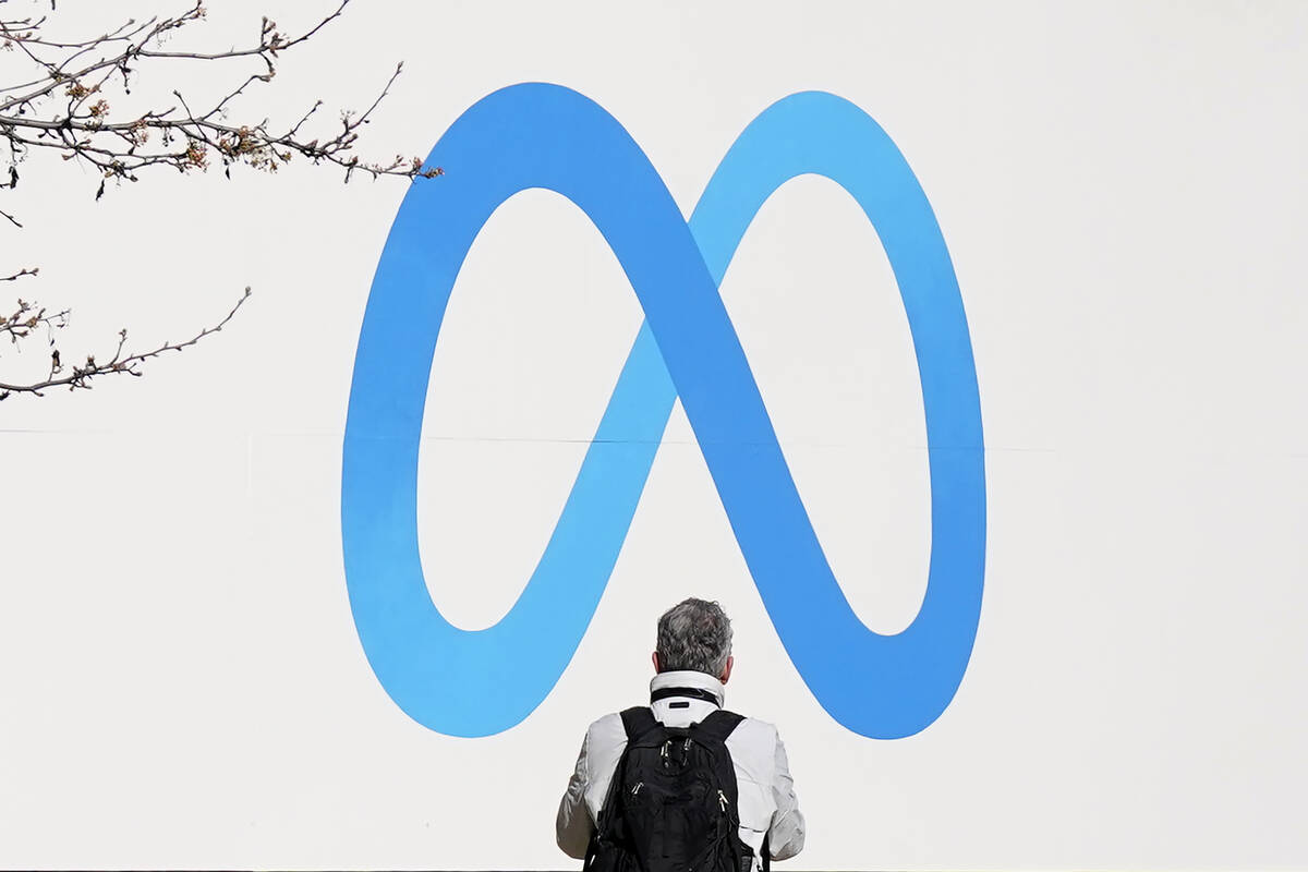 A person stands in front of a Meta sign outside of the company's headquarters in Menlo Park, Ca ...