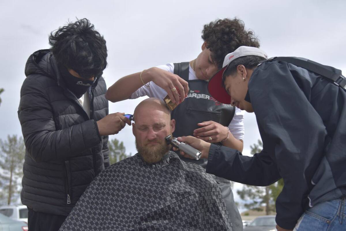 Richy Cruz, left, Gabriel Lopez, middle, and Joshua Polo, right, give a man a free haircut near ...