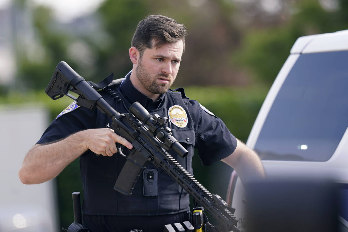 A law enforcement officer carries a rifle as people are evacuated from a shopping center where ...