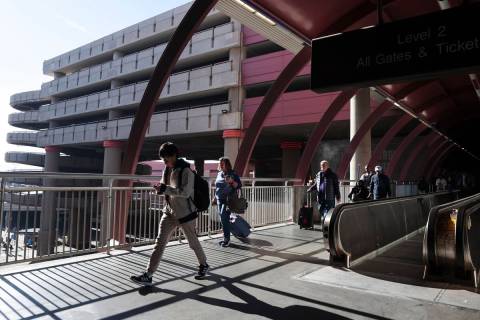 FILE - Travelers walk to the parking garage and ride share pickup area at Harry Reid Internatio ...