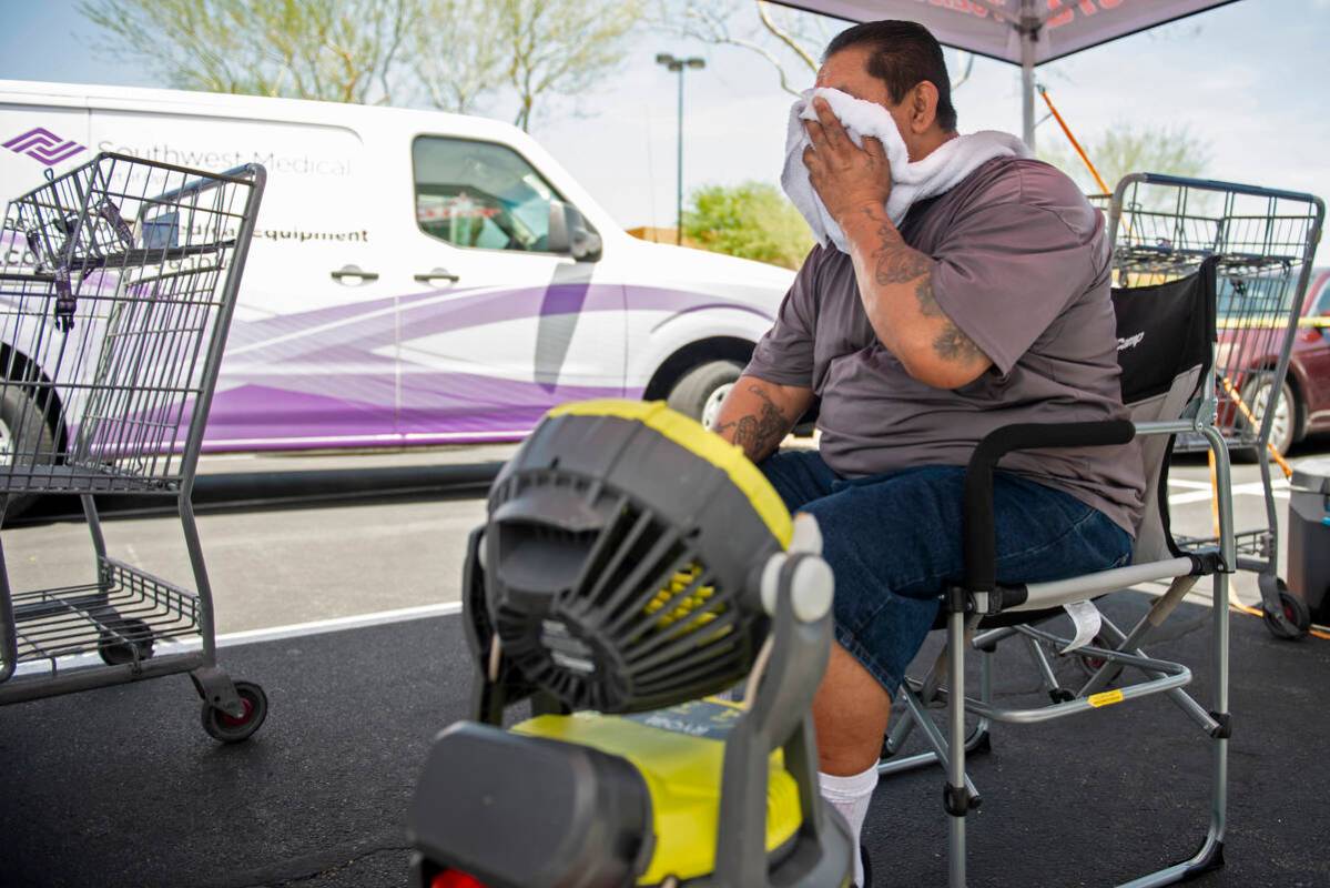 Gus Alvarez cools off with a fan and a bucket of cold water while working at a school supplies ...