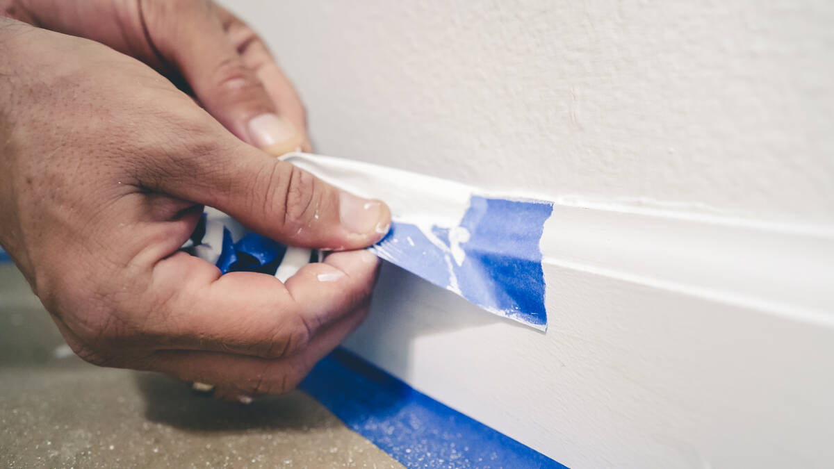 Blue painter’s tape is pulled from the wall to reveal a clean edge baseboard. (Getty Images)
