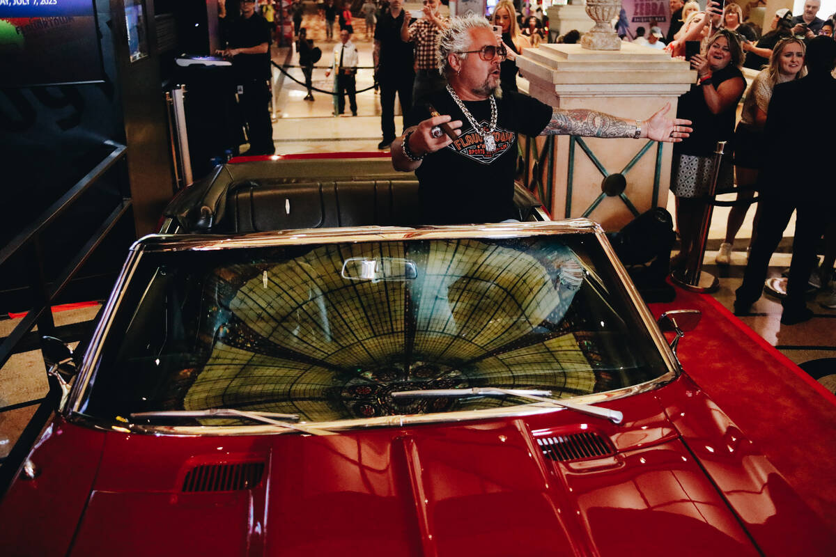 Guy Fieri smokes a cigar and speaks to fans and members of the media while sitting inside of a ...