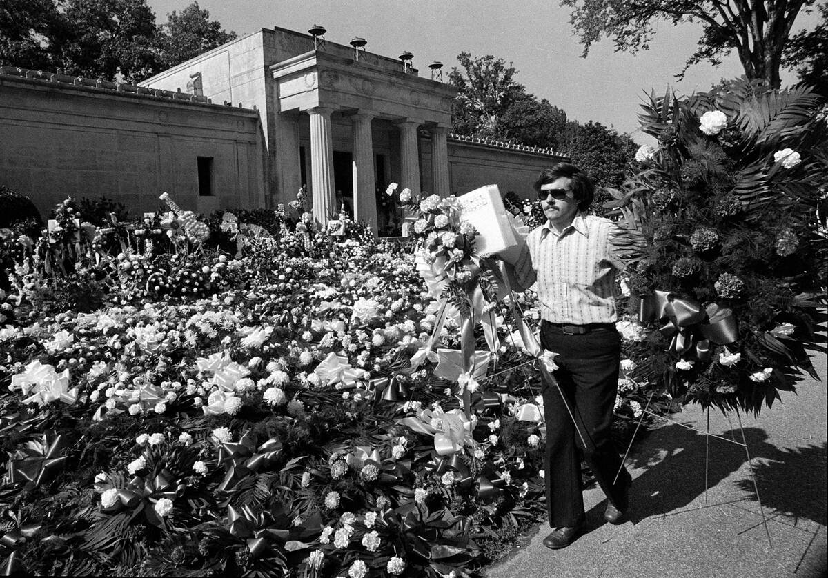 A florist adds more floral arrangements to the overflowing collection of flowers that cover the ...