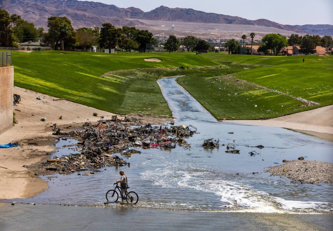 A man with bicycle cross a wash piled with debris moving through The Club at Sunrise, downstrea ...