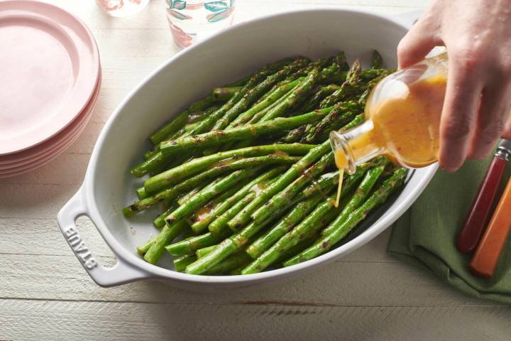 A vinaigrette dressing is poured over grilled asparagus in February 2020. Beyond lettuce salads ...