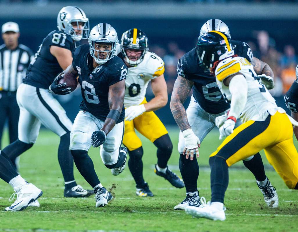 Raiders running back Josh Jacobs (8) bursts through the line as Raiders guard Netane Muti (54) ...