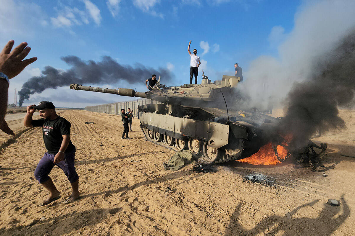 Palestinians celebrate by a destroyed Israeli tank at the Gaza Strip fence east of Khan Younis ...
