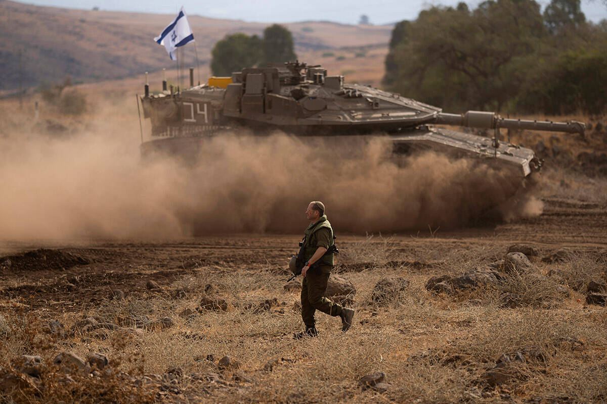 An Israeli soldier walks in front of a moving tank with an Israeli flag on the top in a staging ...