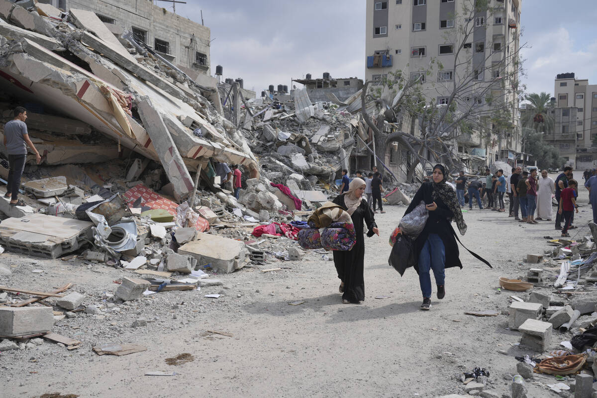 Palestinian women walk by buildings destroyed in Israeli airstrikes in Nuseirat camp in the cen ...