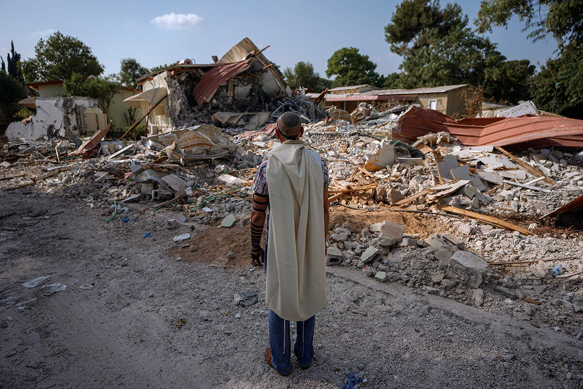An Israeli man wearing a prayer shawl prays next to houses destroyed by Hamas militants in Kibb ...