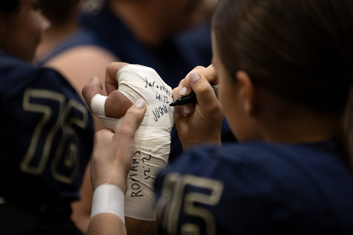 Kicker Gracie Rhodes writes a Bible verse on her teammate Vance Maheu’s taped wrist befo ...