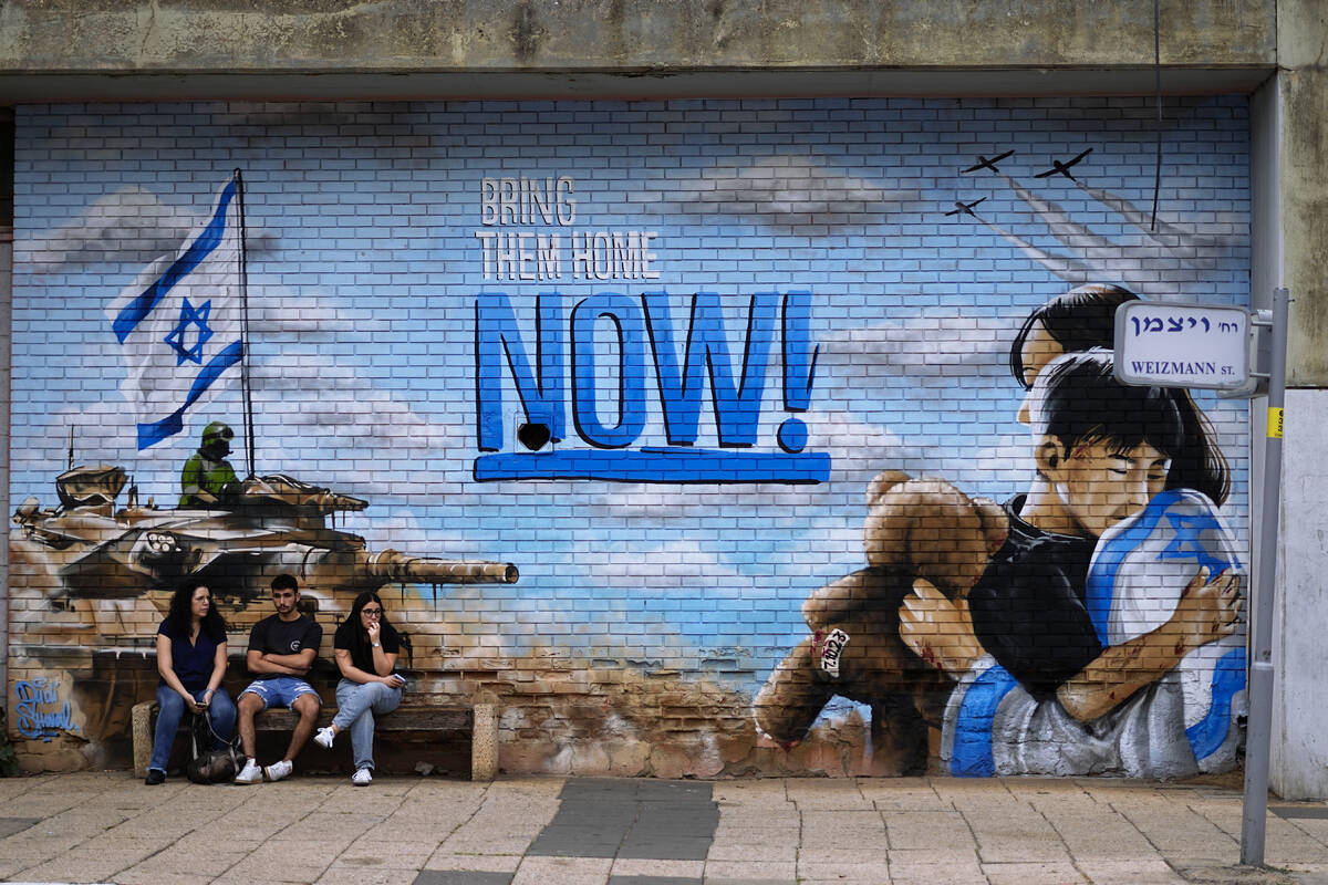 Mourners sit next to graffiti calling for the return of the hostages kidnapped during the Oct. ...