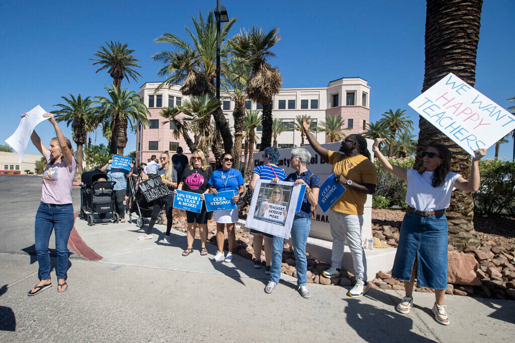 A group of parents and community members hold up signs to support better teacher pay during a r ...