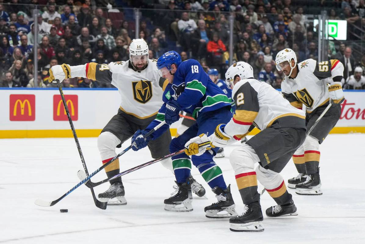 Vancouver Canucks' Sam Lafferty (18) splits Vegas Golden Knights' Nicolas Hague (14) and Zach W ...