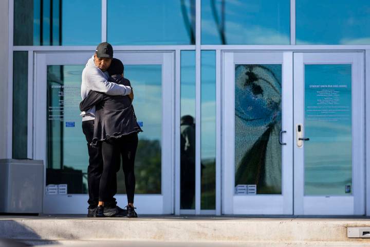 Two people hug near a shattered front door glass panel at the Student Union following the shoot ...