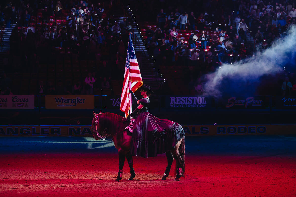 A cowgirl holds the American flag during the national anthem during the NFR opening ceremony at ...