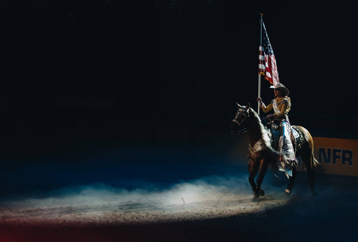 A woman rides a horse during the national anthem during day three of the National Finals Rodeo ...