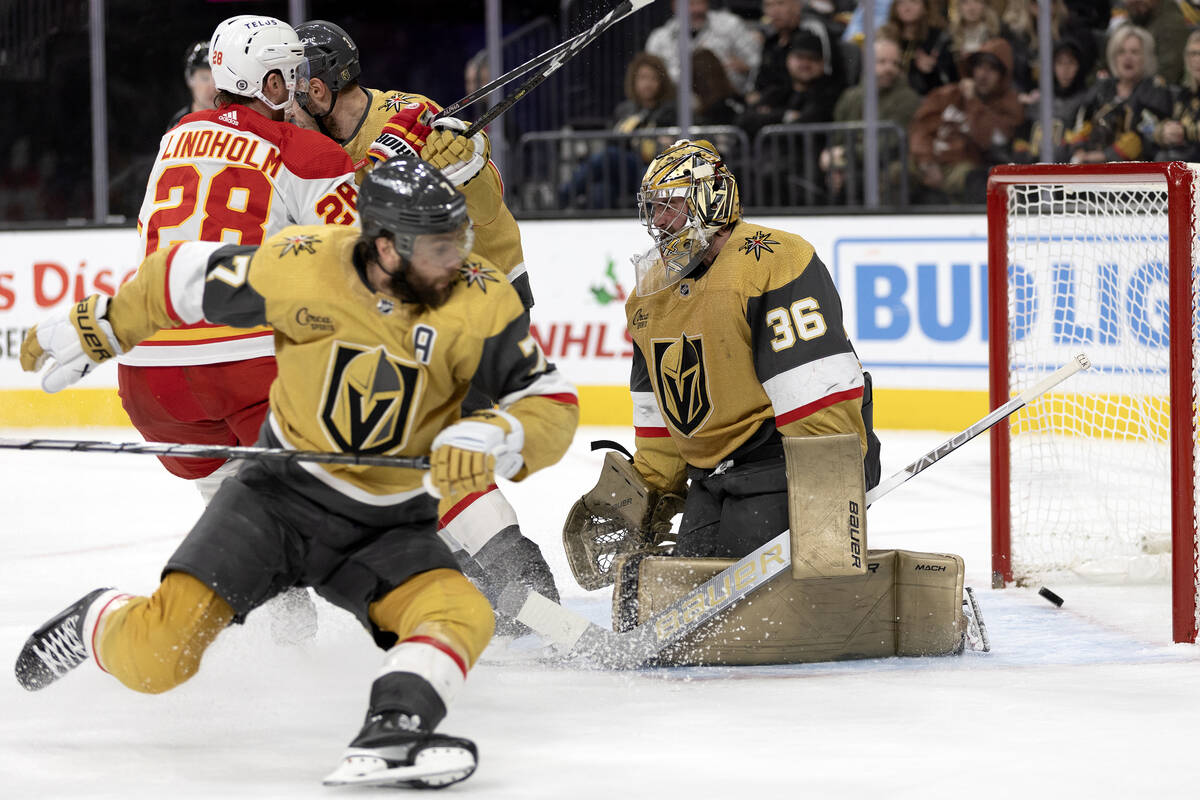 Flames center Elias Lindholm (28) assists a goal while Golden Knights goaltender Logan Thompson ...