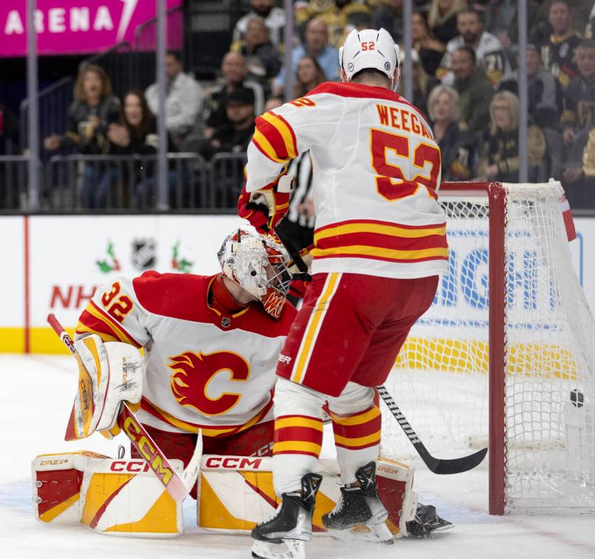 Flames goaltender Dustin Wolf (32) and defenseman MacKenzie Weegar (52) watch the puck in the n ...