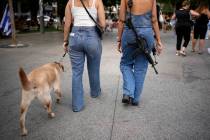 A woman carries an assault rifle as she and a friend walk a dog in downtown Tel Aviv on Nov. 11 ...