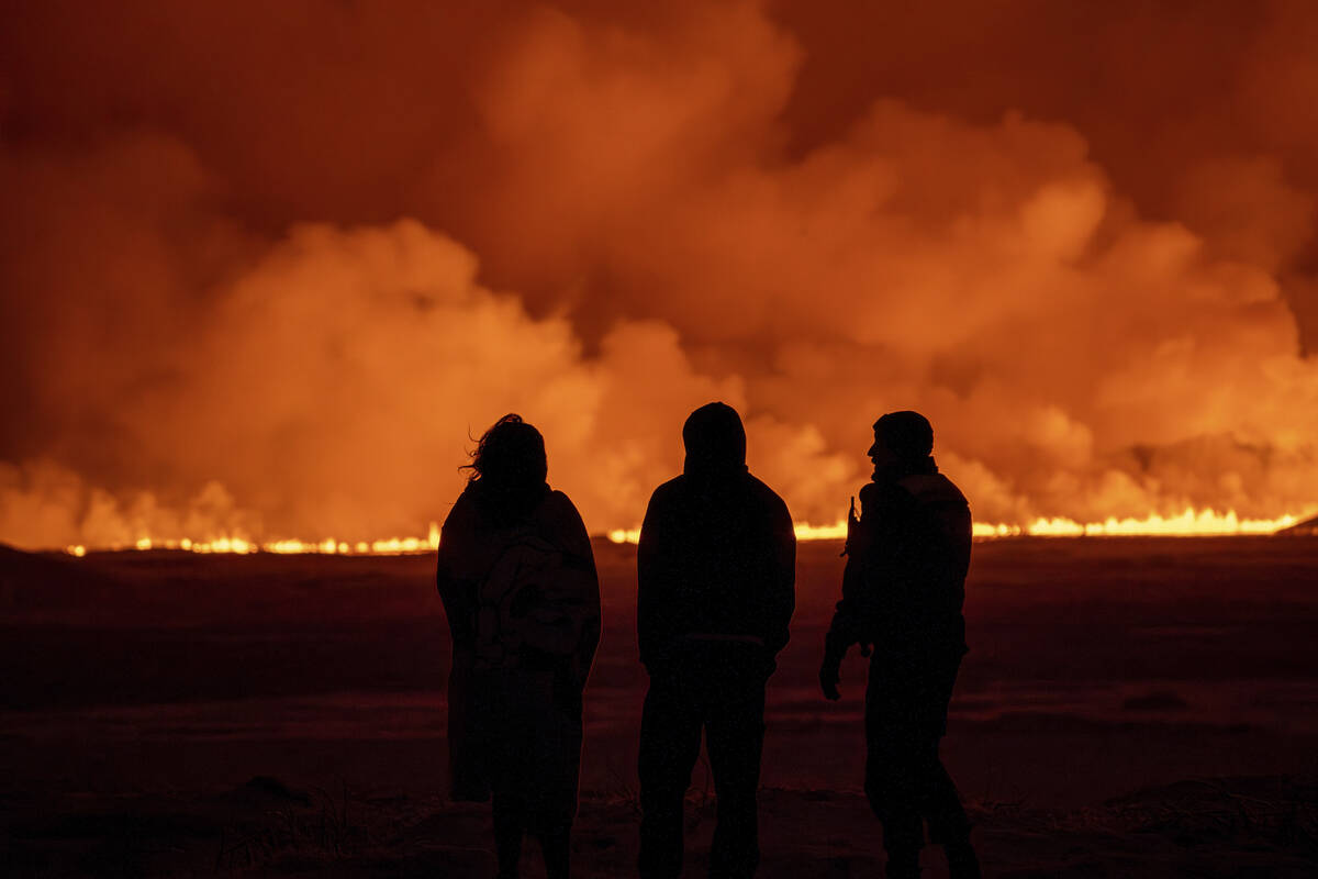 People watch as the night sky is illuminated caused by the eruption of a volcano in Grindavik o ...