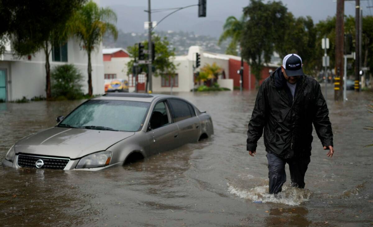 A man walks past a submerged vehicle on a flooded street, Thursday, Dec. 21, 2023, in Santa Bar ...