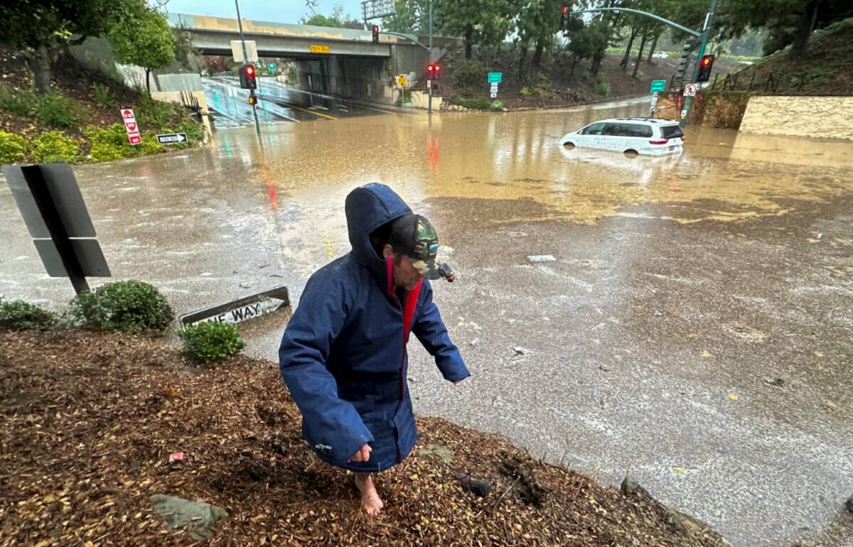 A pedestrian tries to walk around a flooded zone near an overpass as rain comes down, Thursday, ...