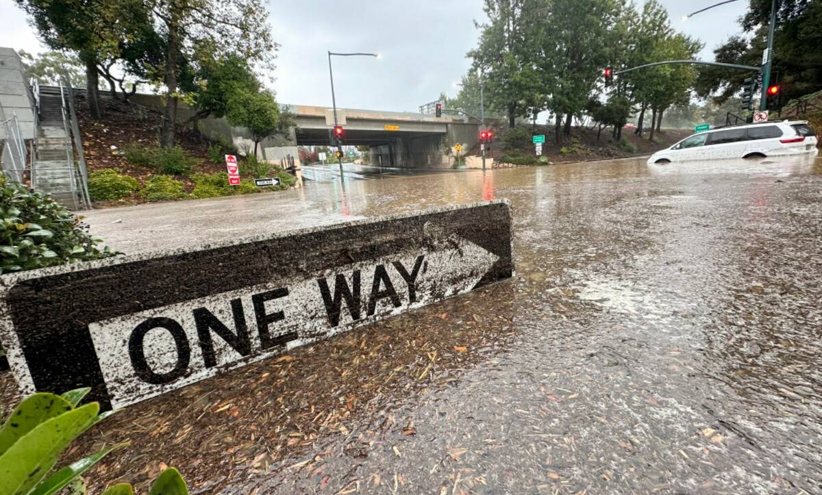 Floodwaters reach the top of a street sign near an overpass as rain comes down, Thursday, Dec. ...