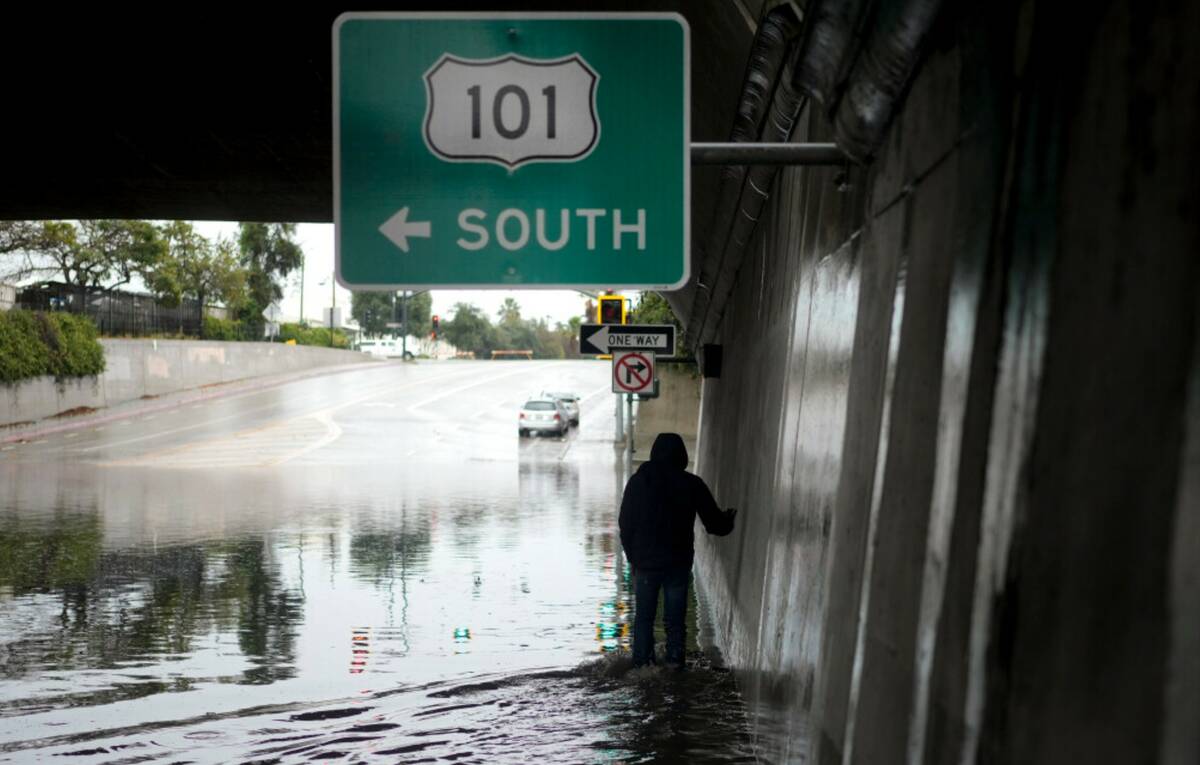 A pedestrian walks under a flooded freeway underpass during a rainstorm, Thursday, Dec. 21, 202 ...