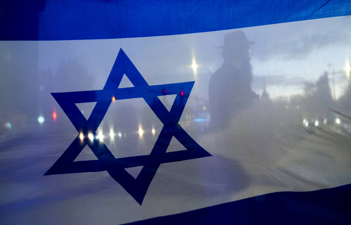 A demonstrator is silhouetted behind a flag of Israel during a rally in support of Israel on Oc ...