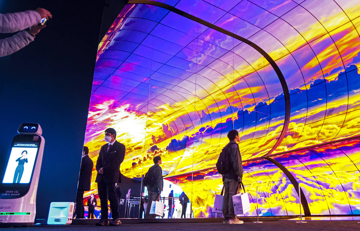 People are silhouetted by an OLED display at the LG booth during the final day of CES at the La ...