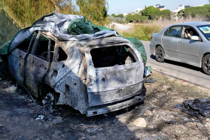 A woman, right, sits in a car and takes pictures of the burned and damaged car that was used by ...